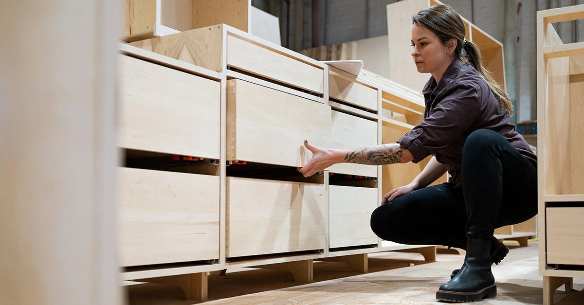 A woman opening a drawer of a preassembled kitchen cabinet at a manufacturing facility.