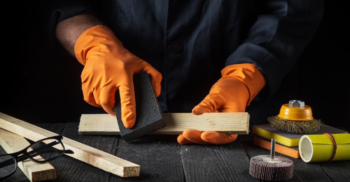 Professional craftsman cleans the wood plank with an abrasive tool. 