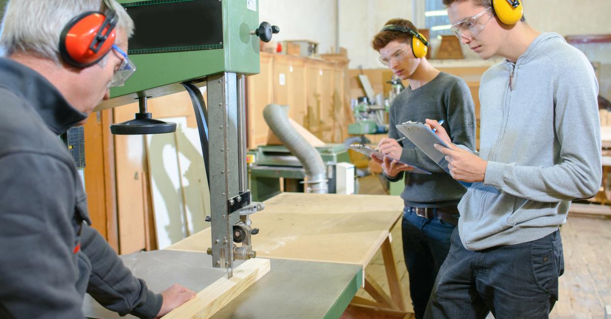 2 woodwoodworking apprentices learning how to use a saw.
