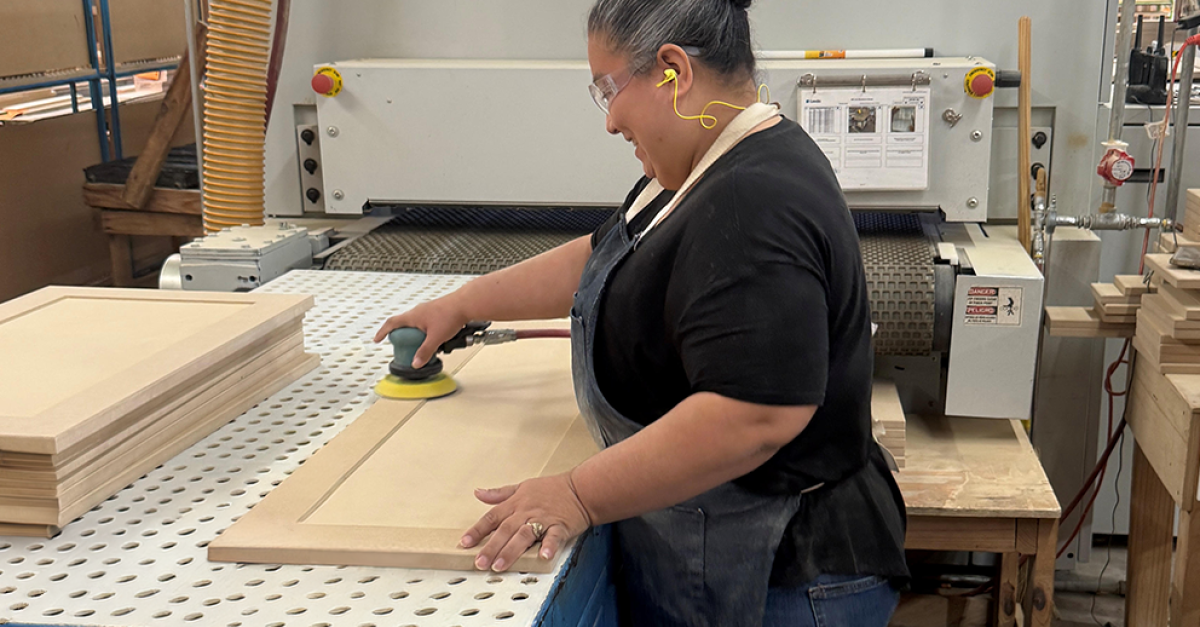 A worker at a cabinet manufacturing facility wearing personal protective equipment (PPE) sands new kitchen cabinet doors.