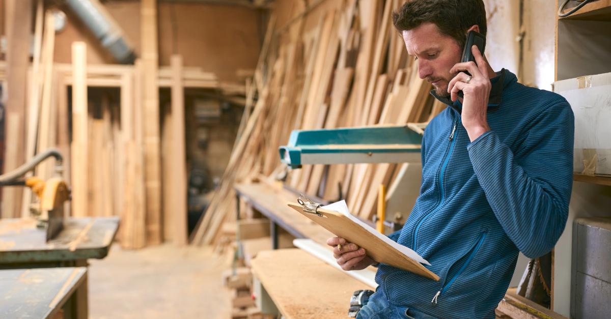 Young man in a woodworking shop using a cell phone.