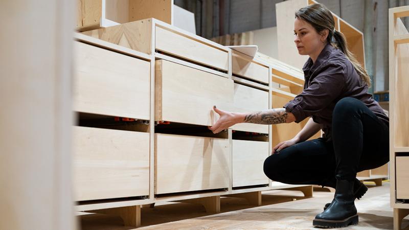 A woman opening a drawer of a preassembled kitchen cabinet at a manufacturing facility.